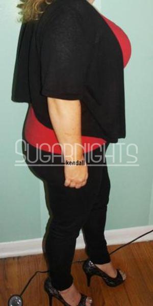 Busty Mature Kendall standing indoors in a red top and black pants